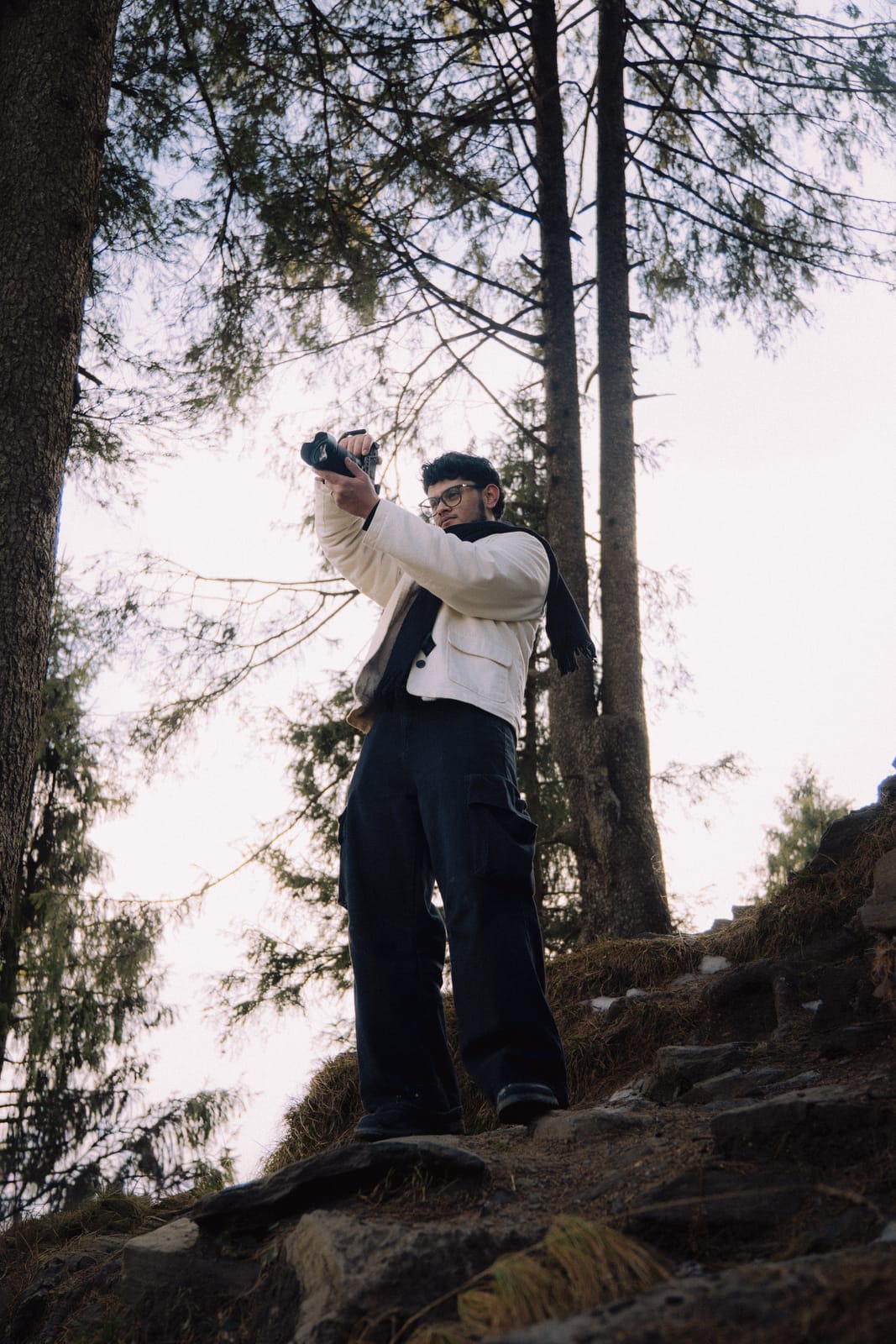 Razan Ahmad taking a photo on a rocky path among tall pine trees